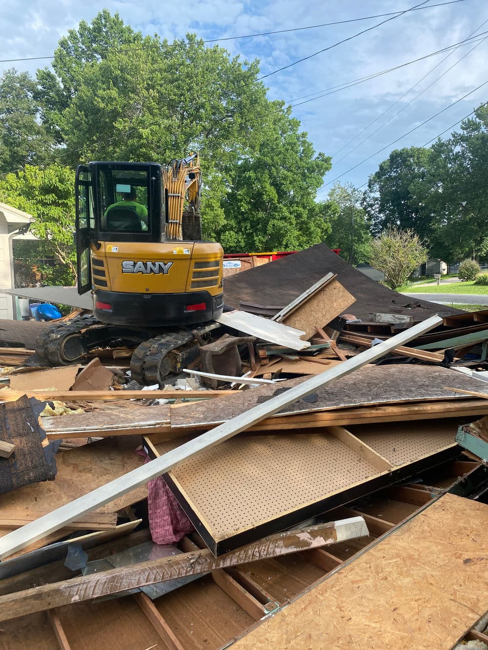 Excavator on a pile of debris from a demolished structure under a blue sky.