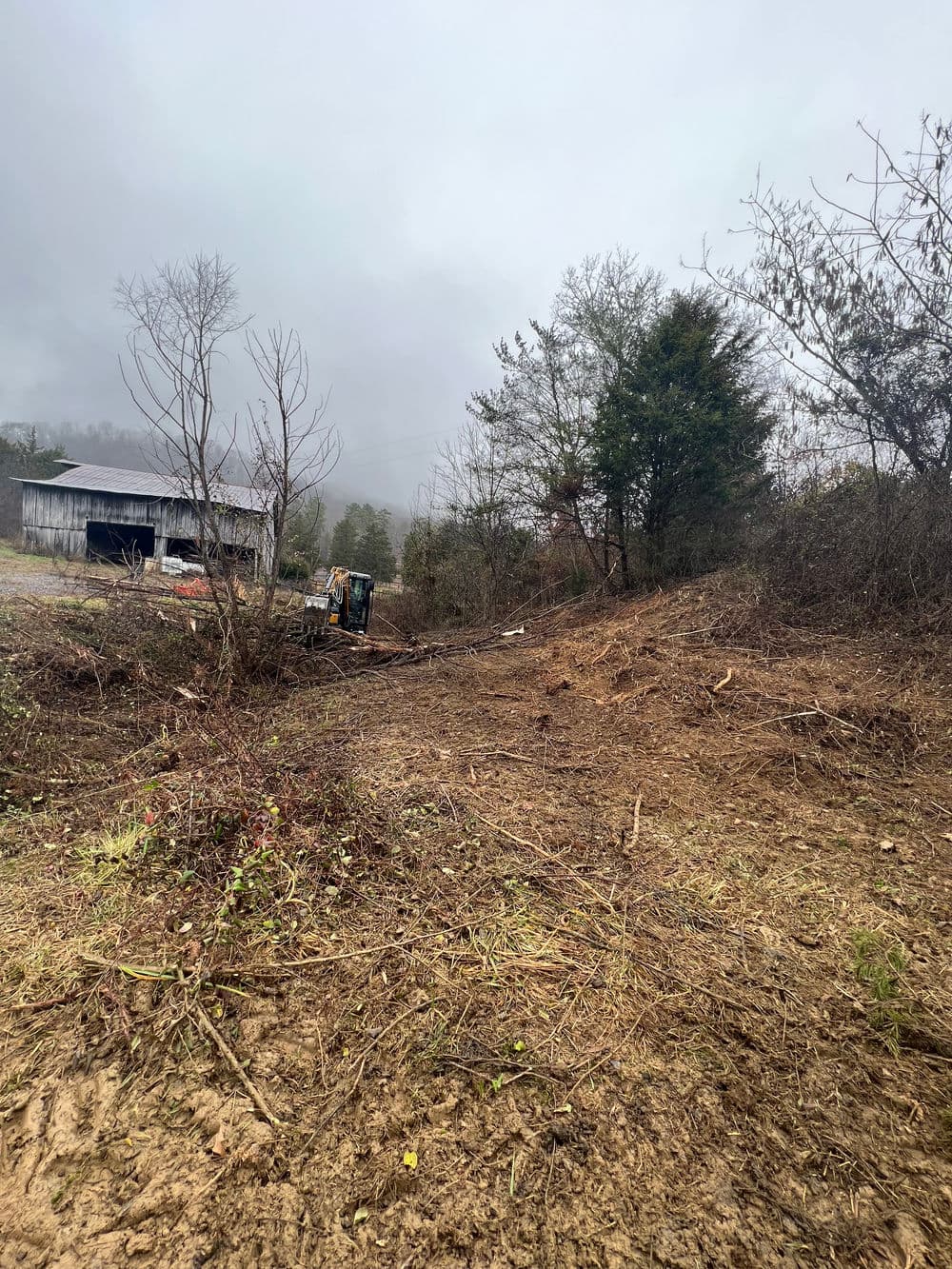 Cleared land with machinery under a cloudy sky near a barn in a rural area.