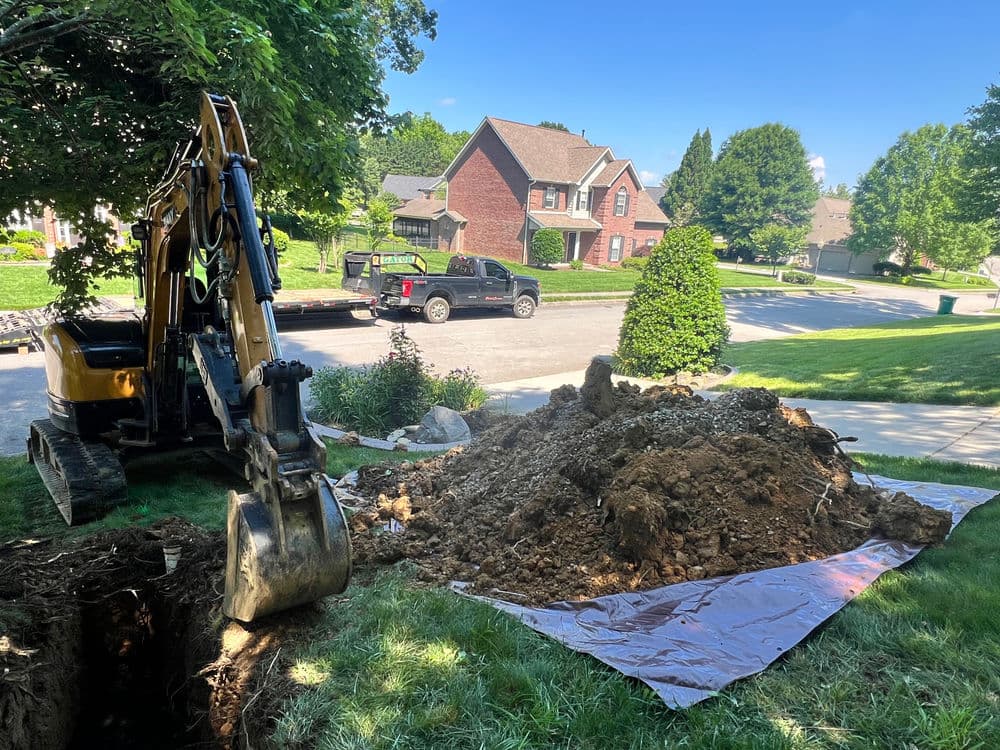 Excavator and dirt pile in residential yard, showcasing landscaping work and nearby homes.