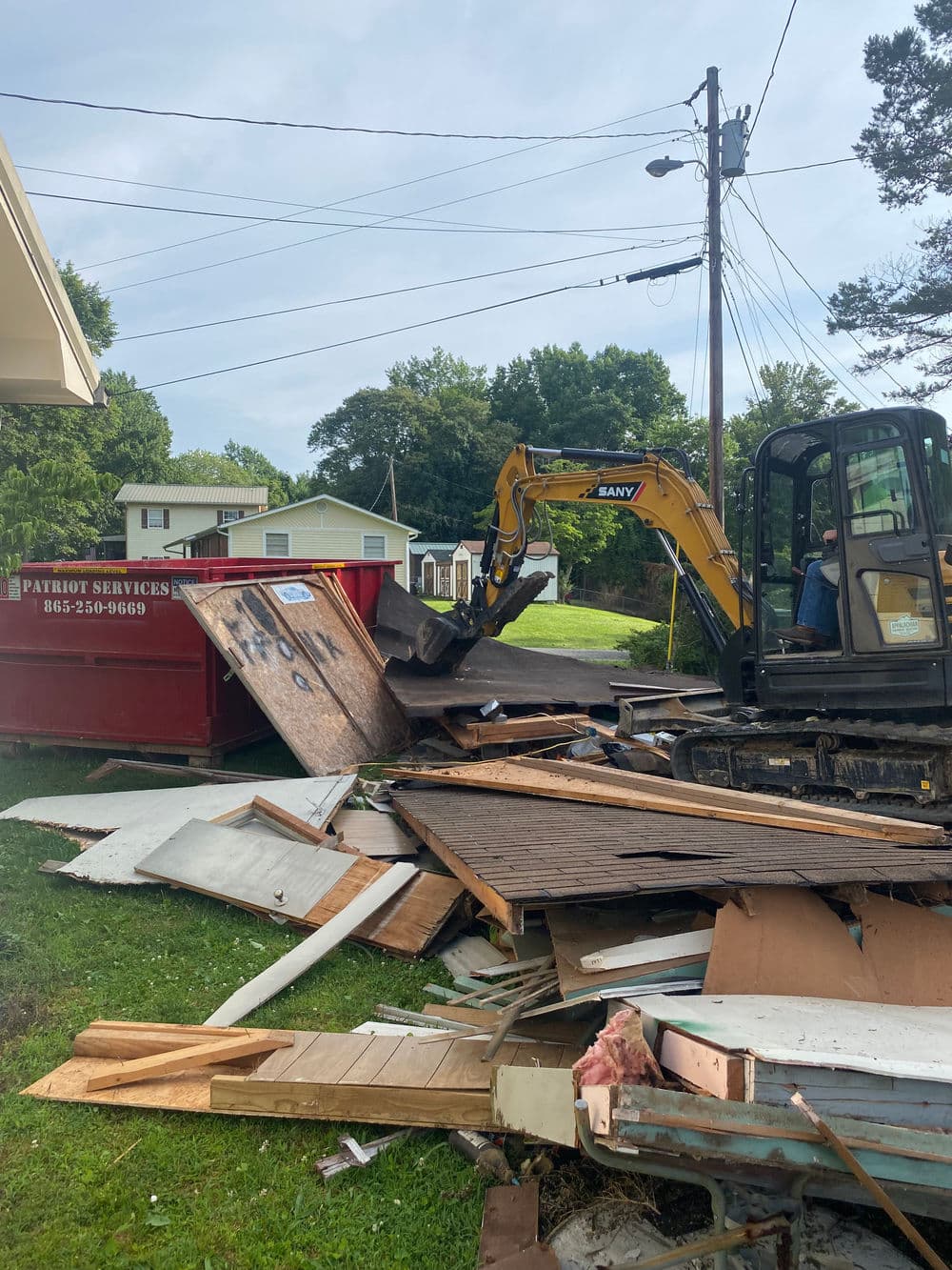 Excavator removing debris near dumpster in residential area during demolition project.