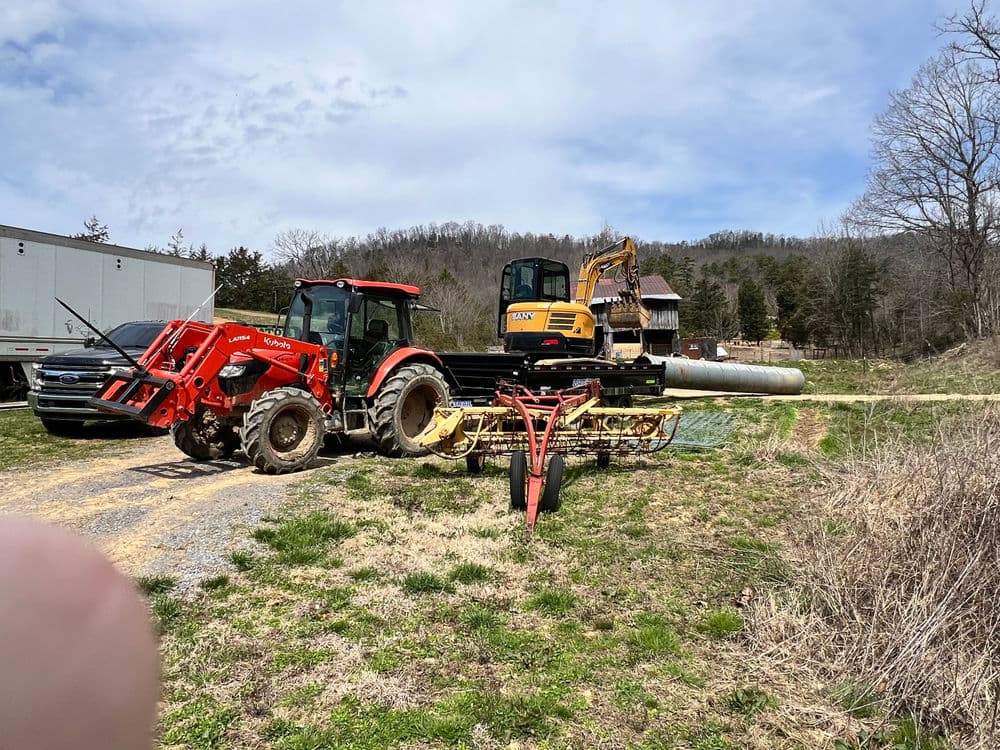 Red tractor and excavator parked on a rural landscape with machinery and trees in the background.