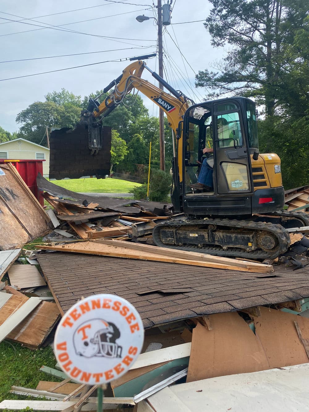 Excavator demolishing building debris with Tennessee Volunteers sign in foreground.